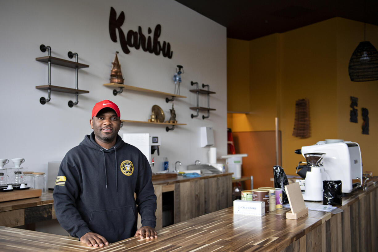 James Mbuya, owner of a new coffee shop in Uptown Village called Richland Hub, takes a break behind the front counter Friday morning. The "Karibu" sign behind him means "Welcome" in Swahili.