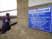 FILE - A man jogs past a sign about crisis counseling on the Golden Gate Bridge in San Francisco, Aug. 3, 2021.  People in crisis and those trying to help them will have a new three-digit number, 988, to reach the national suicide prevention network starting in July. Federal health officials on Monday are announcing more than $280 million to smooth the transition from the current 10-digit number.