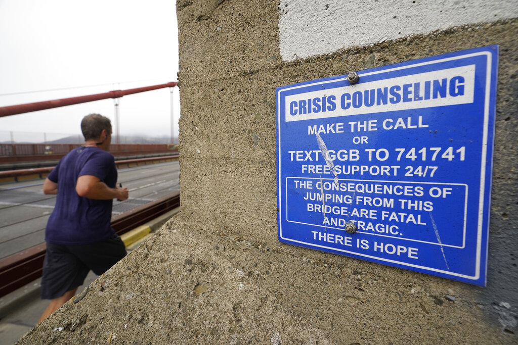 FILE - A man jogs past a sign about crisis counseling on the Golden Gate Bridge in San Francisco, Aug. 3, 2021.  People in crisis and those trying to help them will have a new three-digit number, 988, to reach the national suicide prevention network starting in July. Federal health officials on Monday are announcing more than $280 million to smooth the transition from the current 10-digit number.