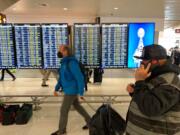 Travelers at Seattle-Tacoma International Airport check the status of flights, including a few that were canceled, on displays inside a gate terminal, Friday, April 1, 2022 in Seattle.  Dozens of flights along the West Coast are being canceled as Alaska Airlines pilots picket during ongoing contract negotiations with the airline.  (AP Photo/Ted S.