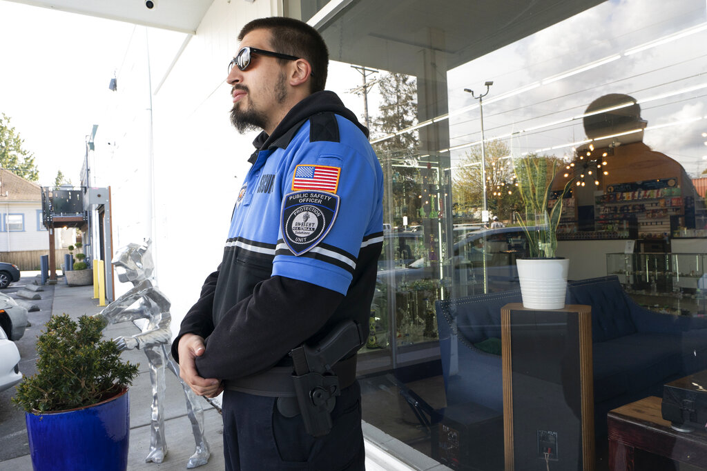 Security guard Austin MacMath wears a gun on his belt, Tuesday, April 19, 2022, while working outside Mary Mart, a marijuana store in Tacoma, Wash. A surge in robberies at licensed cannabis shops in Washington state is helping fuel a renewed push for federal banking reforms that would make the cash-dependent stores a less appealing target. (AP Photo/Ted S.