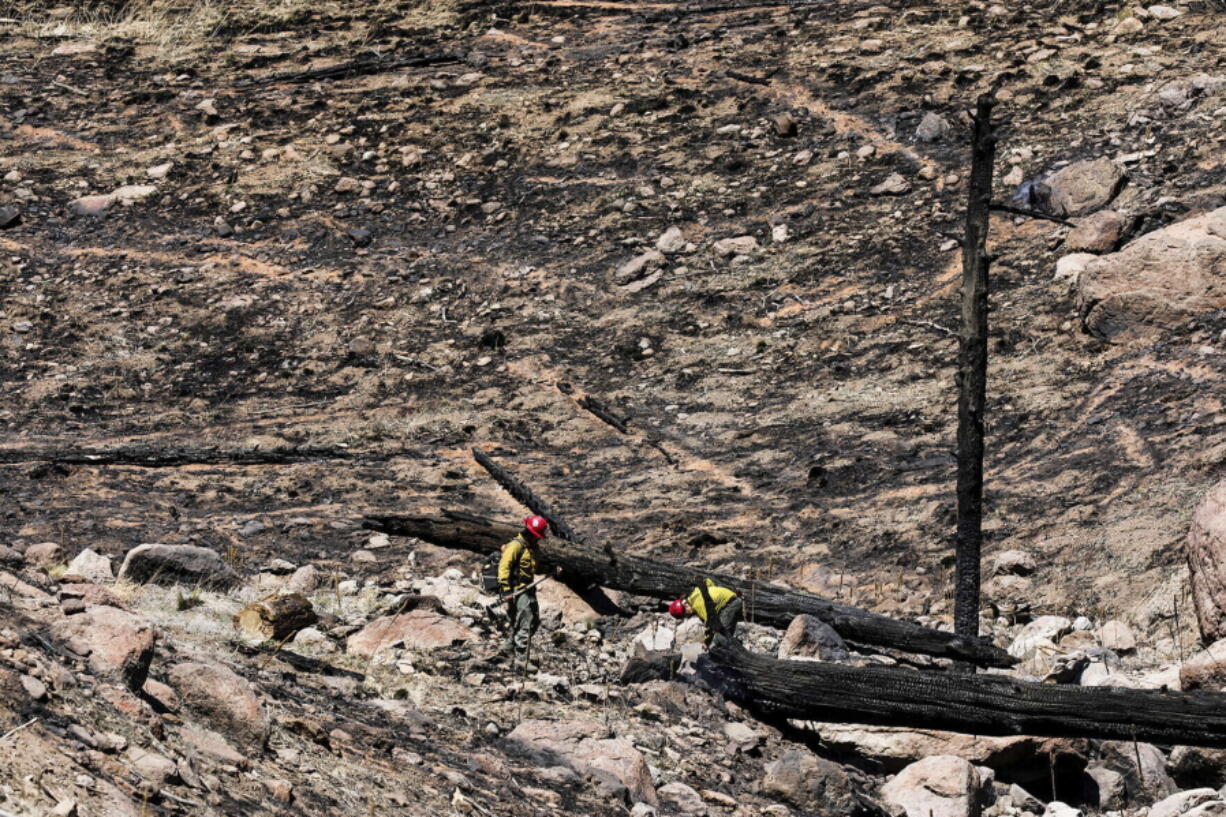 Two firefighters crest a hill as they work to put out hot spots on a wildfire burning on the outskirts of Flagstaff, Ariz., Thursday, April 21, 2022.