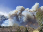 Smoke from a wind-whipped wildfire rises above neighborhoods on the outskirts of Flagstaff, Ariz., on Tuesday, April 19, 2022. Homes on the outskirts of Flagstaff were being evacuated Tuesday as high winds whipped a wildfire, shut down a major highway and grounded firefighting aircraft.