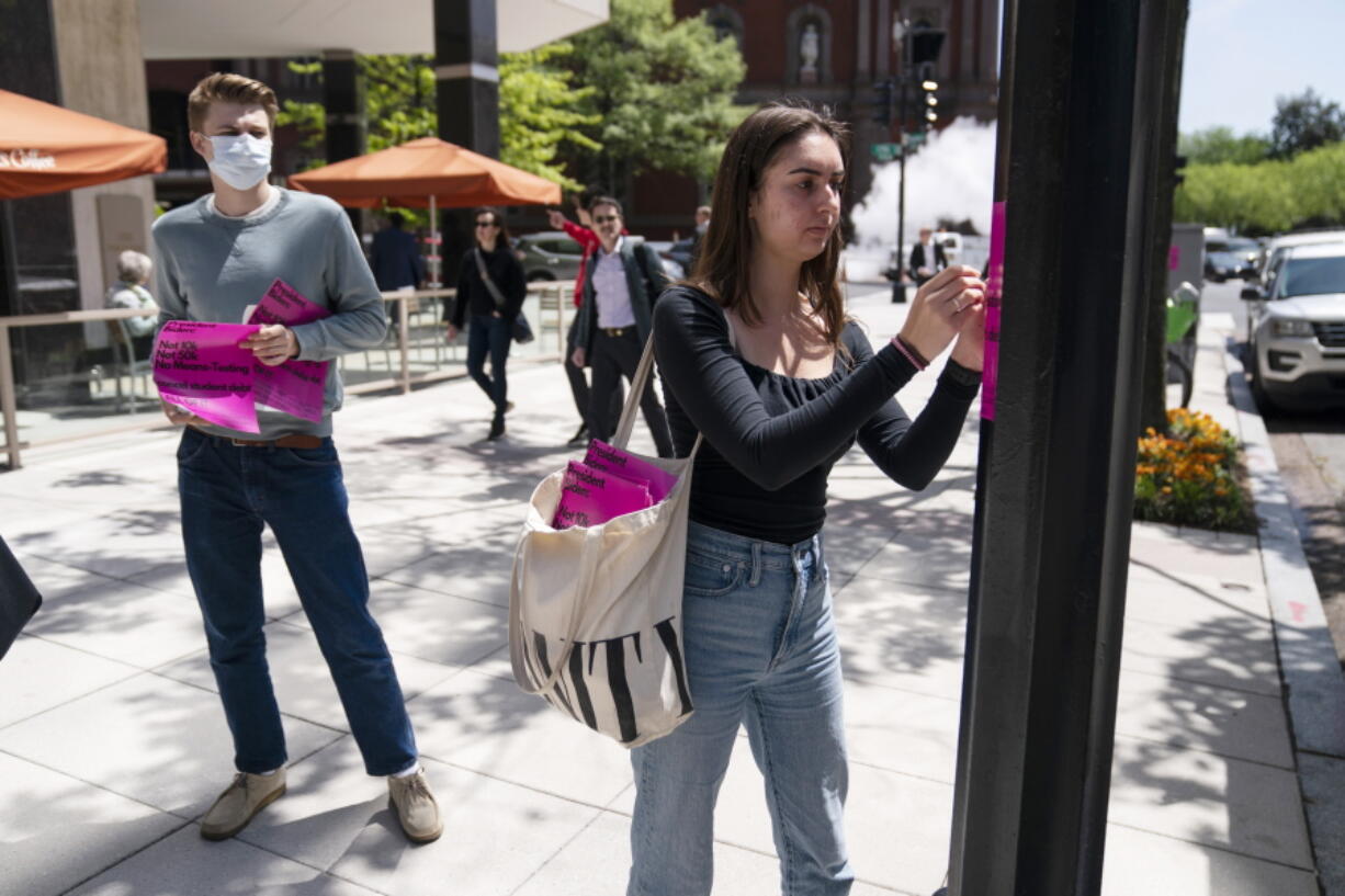 George Washington University student Kai Nilsen, left, watches as American University student Magnolia Mead as they put up posters near the White House promoting student loan debt forgiveness, Friday, April 29, 2022, in Washington.