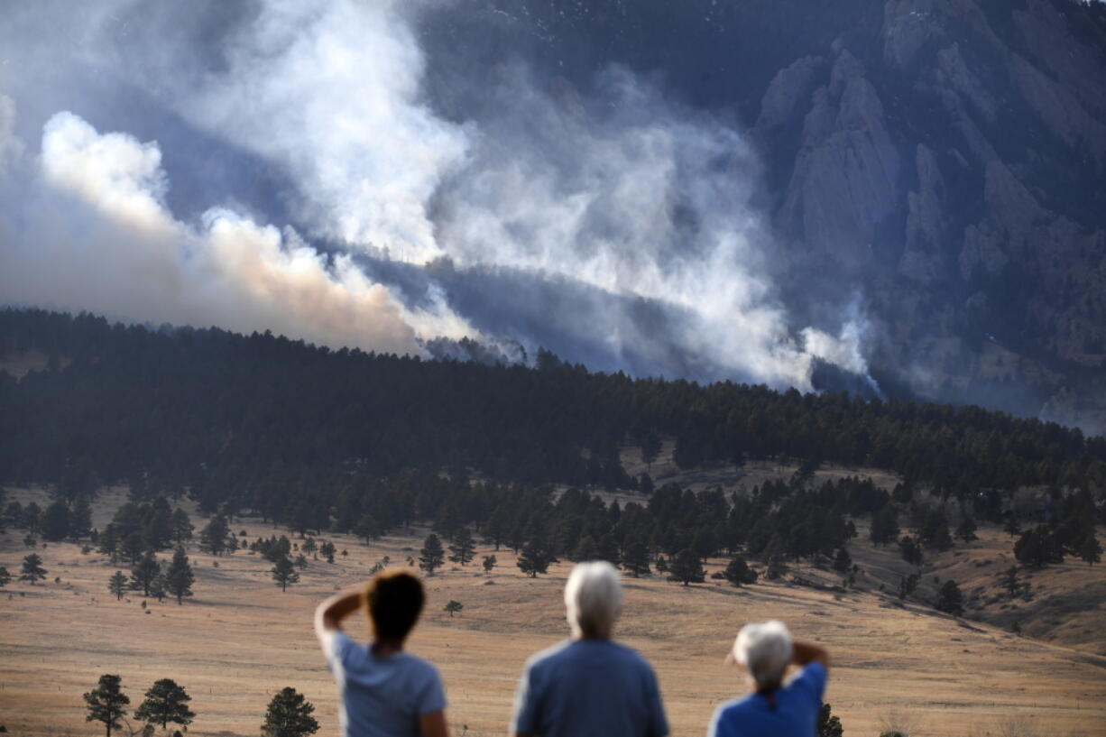 From left, Laura Tyson, Tod Smith and Rebecca Caldwell, residents of Eldorado Springs, watch as the NCAR fire burns in the foothills south of the National Center for Atmospheric Research, Saturday, March 26, 2022, in Boulder, Colo. The NCAR fire prompted evacuations in south Boulder and pre-evacuation warning for Eldorado Springs. According to a study published in Science Advances on Friday, April 1, 2022, a one-two punch of nasty wildfires followed by heavy downpours, triggering flooding and mudslides, will strike the U.S. West far more often in a warming-hopped world, becoming a frequent occurrence. (Helen H.