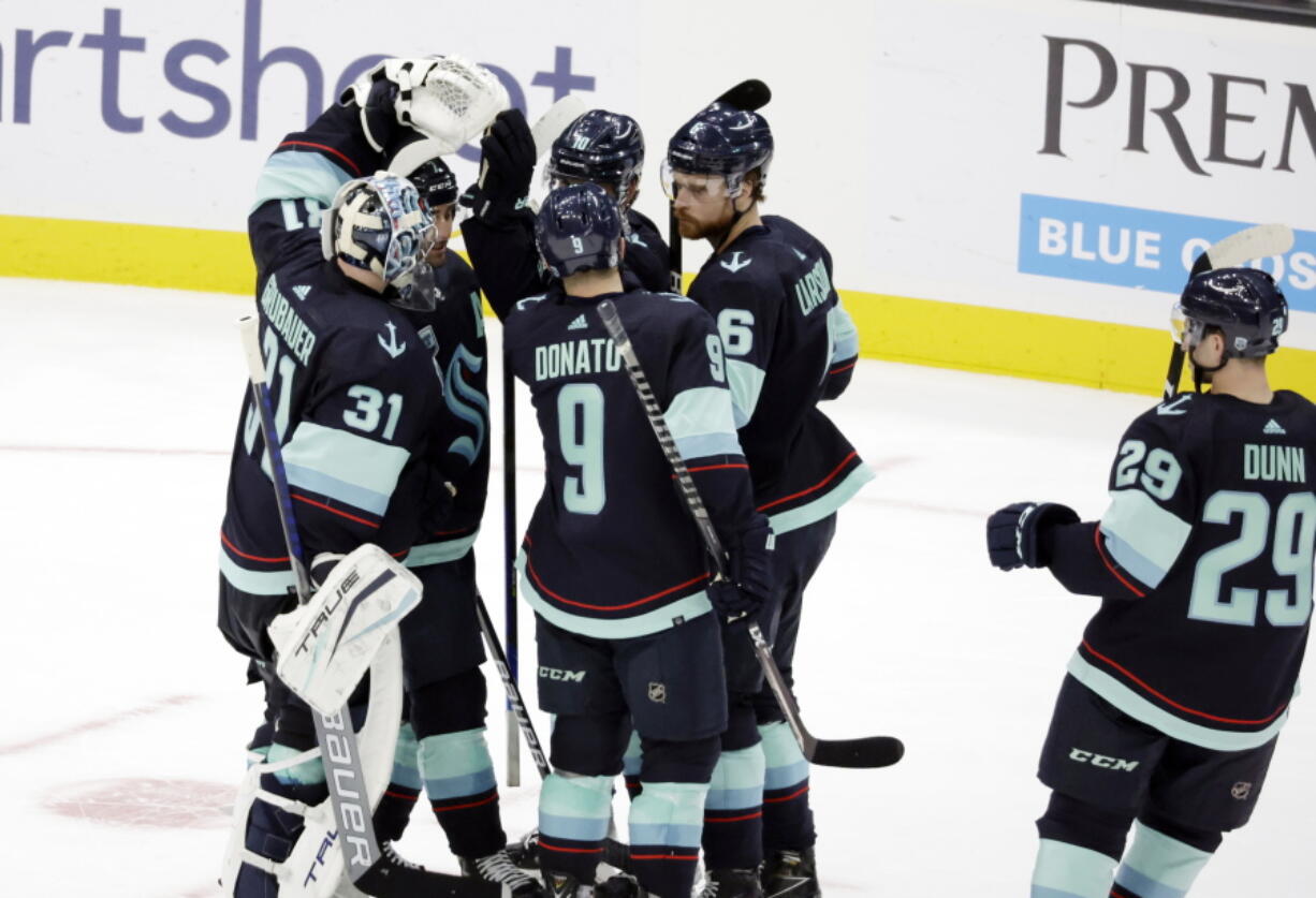 Seattle Kraken players, including goaltender Philipp Grubauer (31), center Ryan Donato (9) defenseman Adam Larsson (6) and defenseman Vince Dunn (29), celebrate the the team's shootout win over the New Jersey Devils in an NHL hockey game Saturday, April 16, 2022, in Seattle.