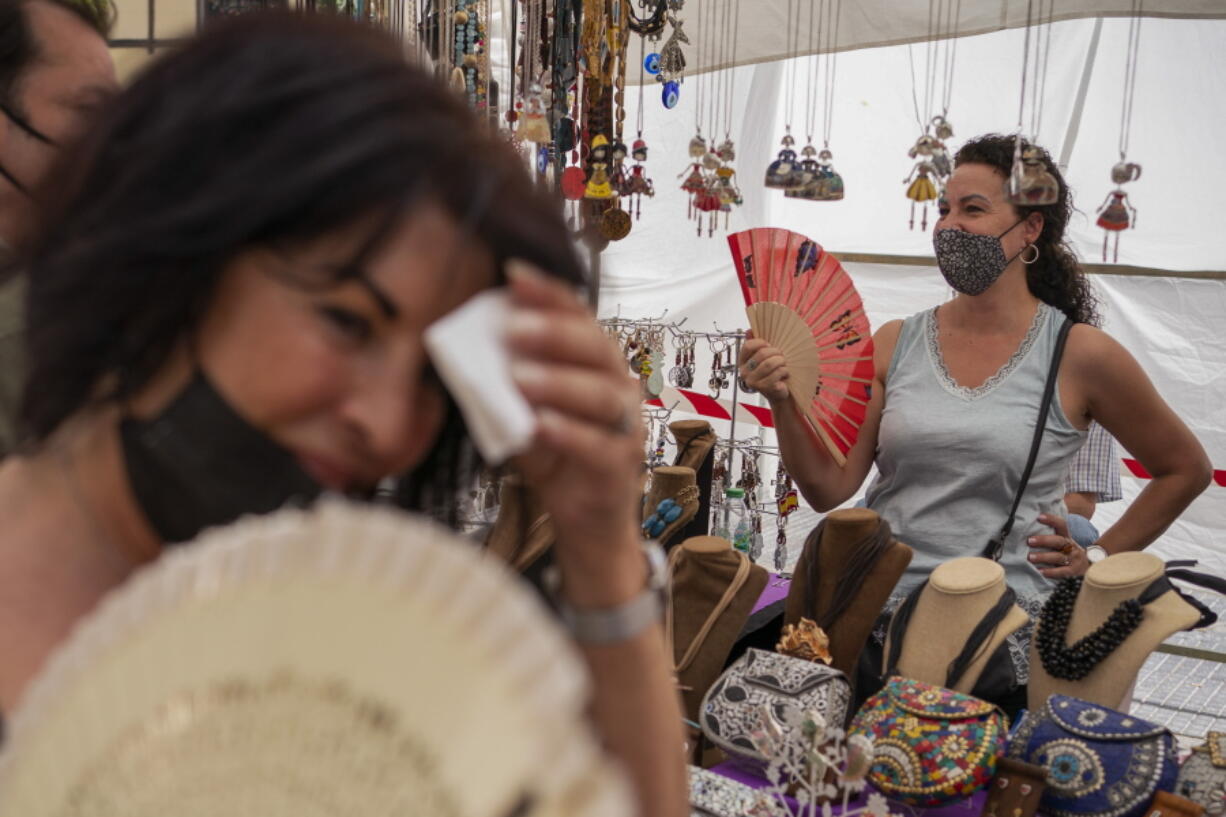 FILE - Women cool themselves with fans in the Rastro flea market during a heatwave in Madrid, Spain, Aug. 15, 2021. Scientists say last summer was the hottest summer on record in Europe, with temperatures a 1.8 Fahrenheit higher than the average for the previous three decades.