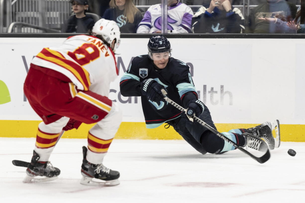 Seattle Kraken forward Ryan Donato, left, goes to ice as he passes the puck in front of Calgary Flames defenseman Christopher Tanev during the second period of an NHL hockey game, Saturday, April 9, 2022, in Seattle.