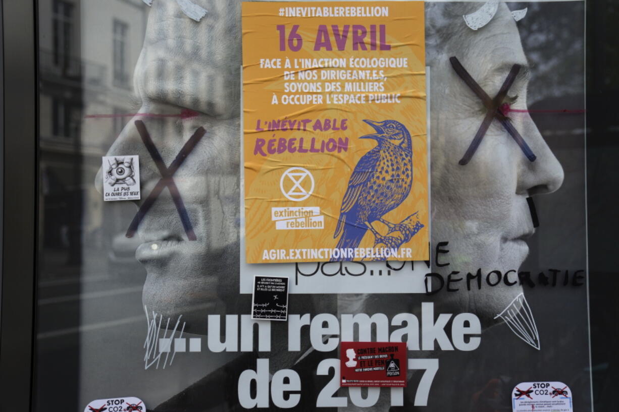 FILE - A torn front page ad shows incubent President Emmanuel Macron and challenger Marine Le Pen as the environmental group Extinction Rebellion takes part in a three-day demonstration against what they call France's inaction on climate issues, in the district of Porte de Saint Denis in the center of Paris, France, Monday, April 18, 2022. French President Emmanuel Macron is in pole position to win reelection Sunday, April 24, 2022 in France's presidential runoff. Yet his lead over far-right rival Marine Le Pen depends on one major uncertainty: voters who decide to stay home. A victory in Sunday's runoff vote would make Macron the first French president in 20 years to win a second term.