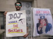 FILE - Nicholas Rivers of Maine, holds a sign that reads DOJ Hammer the Sacklers" during a protest with advocates for opioid victims outside the Department of Justice, Friday, Dec. 3, 2021, in Washington. A federal appeals panel is scheduled to hear arguments on whether members of the Sackler family can be granted protection from lawsuits as part of a bankruptcy settlement for the company they own, OxyContin maker Purdue Pharma. If the company doesn't get what it wants, it could have to fight off thousands of individual lawsuits.