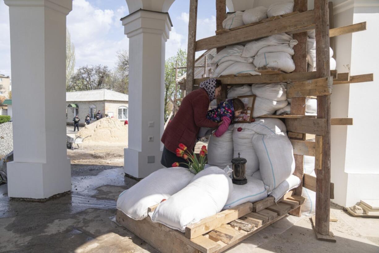 An Orthodox believer helps her daughter to kiss a photo of a priest, founder of All Saints church during the Easter celebration in Bahmut, eastern Ukraine, Sunday, April 24, 2022.