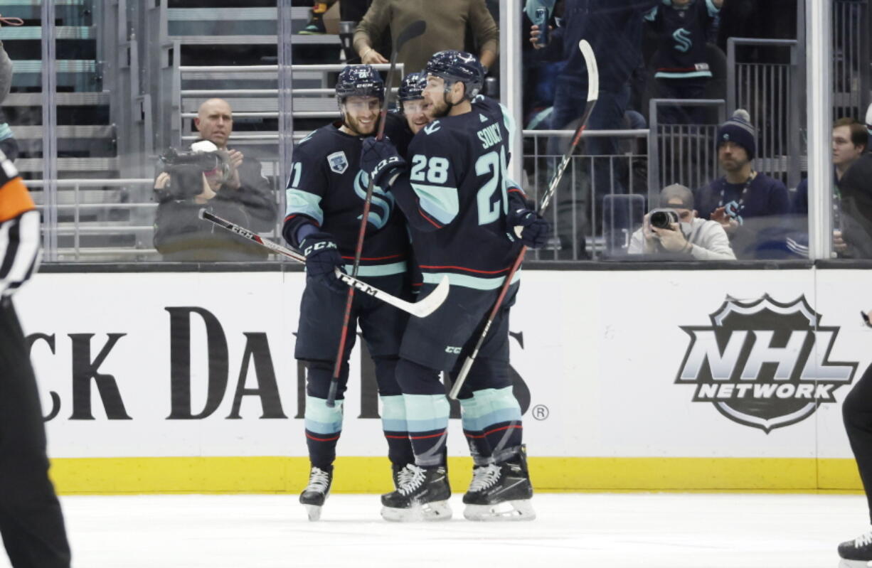 Seattle Kraken center Alex Wennberg, left and defenseman Carson Soucy (28) embrace left wing Jared McCann after he scored against the Dallas Stars during the first period of an NHL hockey game Sunday, April 3, 2022, in Seattle.