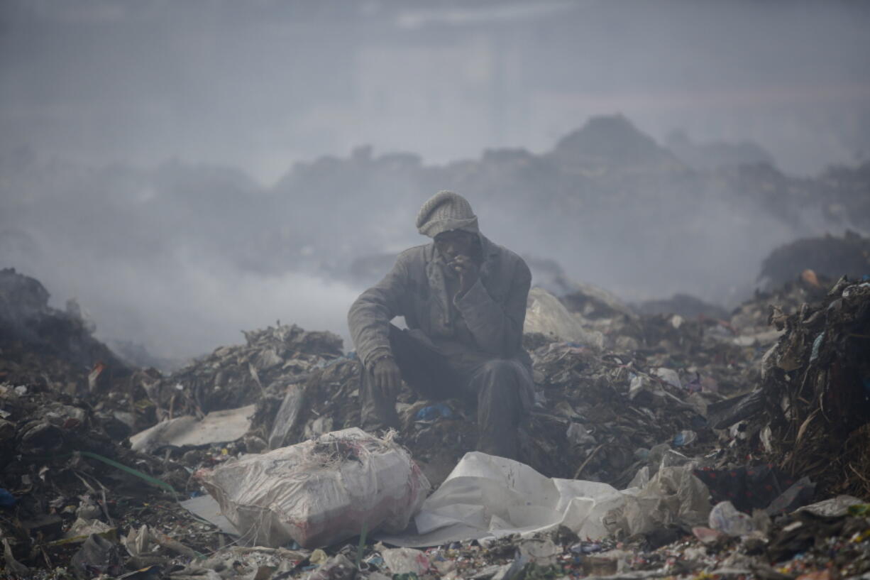 FILE - A man who scavenges recyclable materials for a living rests to smoke a cigarette on a mountain of garage amidst smoke from burning trash at Dandora, the largest garbage dump in the capital Nairobi, Kenya, Tuesday, Sept. 7, 2021. The U.N. health agency said Monday, April 4, 2022, nearly everybody in the world breathes air that doesn't meet its standards for air quality, calling for more action to reduce fossil-fuel use, which generates pollutants that cause respiratory and blood-flow problems and lead to millions of preventable deaths each year.