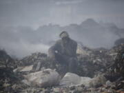 FILE - A man who scavenges recyclable materials for a living rests to smoke a cigarette on a mountain of garage amidst smoke from burning trash at Dandora, the largest garbage dump in the capital Nairobi, Kenya, Tuesday, Sept. 7, 2021. The U.N. health agency said Monday, April 4, 2022, nearly everybody in the world breathes air that doesn't meet its standards for air quality, calling for more action to reduce fossil-fuel use, which generates pollutants that cause respiratory and blood-flow problems and lead to millions of preventable deaths each year.