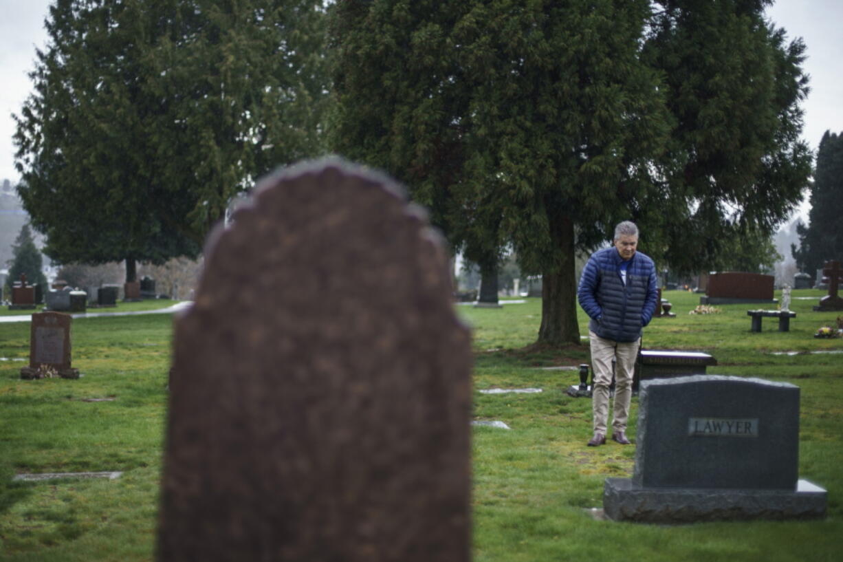 David Lawyer visits the grave of his father, Neil Lawyer, for the first time since the inscription went up on his tombstone in Seattle, Sunday, March 20, 2022. In February 2020, an unfamiliar respiratory illness started spreading through an area nursing home, the Life Care Center of Kirkland. Lawyer, 84, was a short-term patient there and had joined other residents for a belated Mardi Gras party. Days later Lawyer and others fell ill. "By the time he got to the hospital they allowed us to put on these space suits and go in and see him," son David Lawyer says.