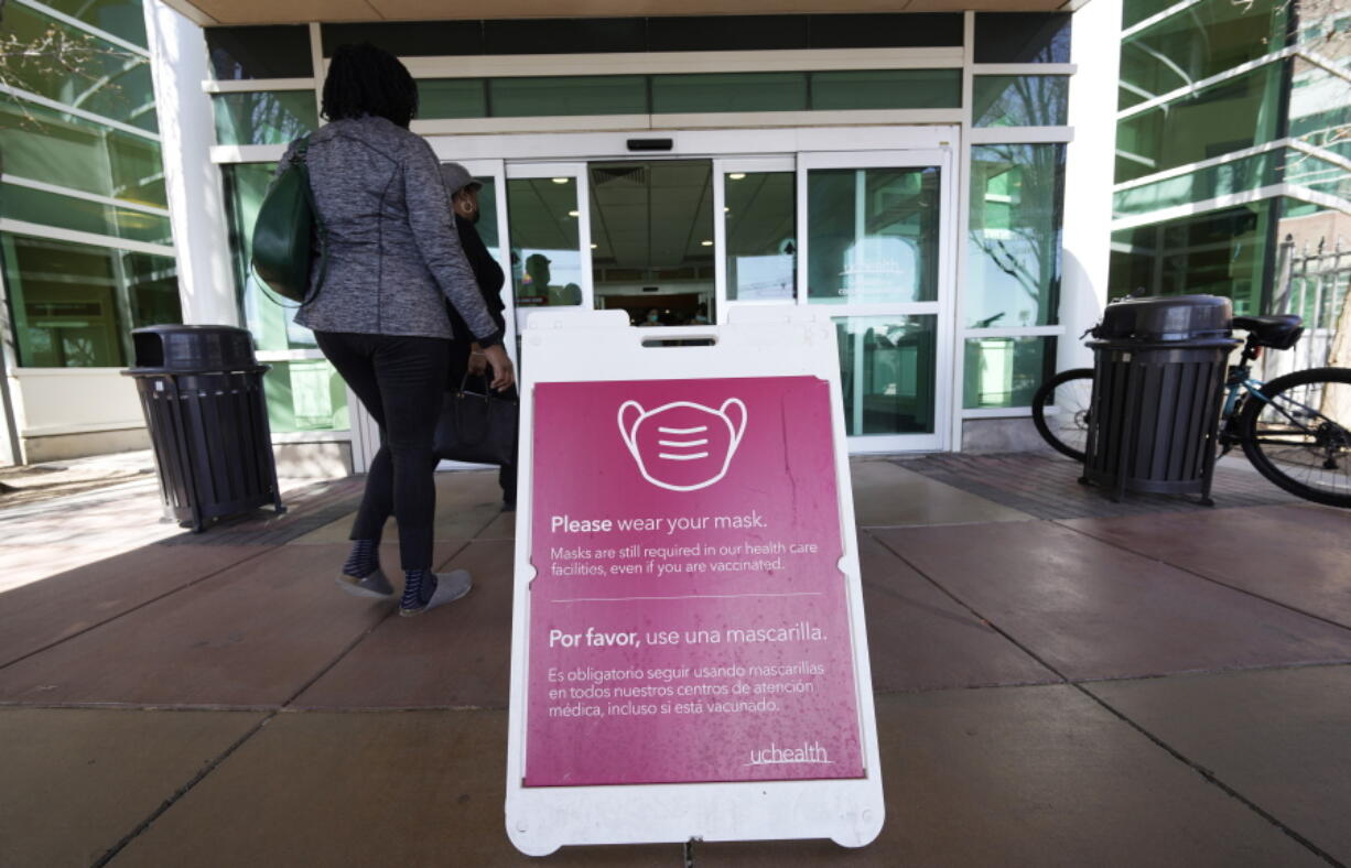 FILE - A sign advising visitors to don face coverings stands outside the main entrance to UCHealth University of Colorado hospital Friday, April 1, 2022, in Aurora, Colo.  COVID cases are starting to rise again in the United States, with numbers up in most states and up steeply in several. One expert says he expects more of a "bump" than the monstrous surge of the first omicron wave, but another says it's unclear how high the curve will rise and it may be more like a hill.