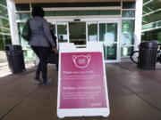 FILE - A sign advising visitors to don face coverings stands outside the main entrance to UCHealth University of Colorado hospital Friday, April 1, 2022, in Aurora, Colo.  COVID cases are starting to rise again in the United States, with numbers up in most states and up steeply in several. One expert says he expects more of a "bump" than the monstrous surge of the first omicron wave, but another says it's unclear how high the curve will rise and it may be more like a hill.