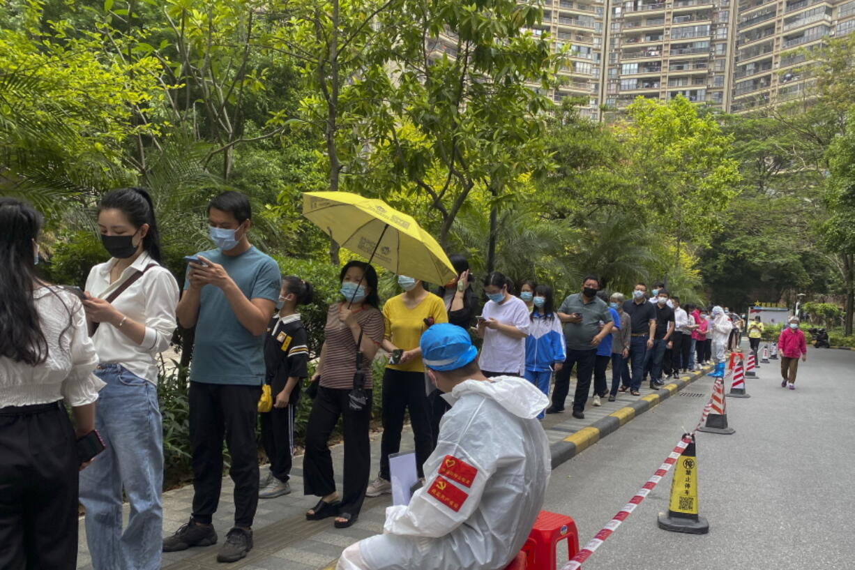 Workers in protective gear watch over residents line up for the COVID-19 test at a residential block, Monday, April 11, 2022, in Guangzhou in south China's Guangdong province. The manufacturing hub of Guangzhou began tightly restricting departures and arrivals Monday as eastern China battles the country's latest major COVID outbreak.