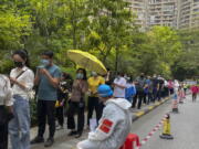 Workers in protective gear watch over residents line up for the COVID-19 test at a residential block, Monday, April 11, 2022, in Guangzhou in south China's Guangdong province. The manufacturing hub of Guangzhou began tightly restricting departures and arrivals Monday as eastern China battles the country's latest major COVID outbreak.