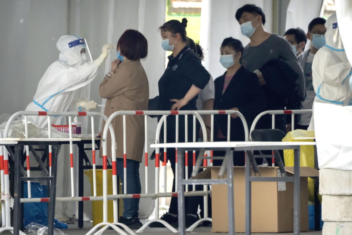 A worker in a protective takes a swab for a COVID-19 test at a coronavirus testing facility in Beijing, Saturday, April 23, 2022. Beijing is on alert after 10 middle school students tested positive for COVID-19 on Friday, in what city officials said was an initial round of testing.