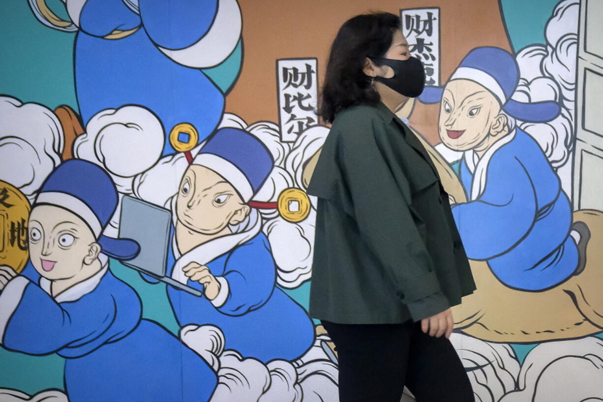 A woman wearing a face mask walks past a mural in Beijing, Friday, April 22, 2022. Officials in Shanghai promised Friday to ease anti-virus controls on truck drivers that are hampering food supplies and trade as they try to revive the local economy while millions of people are still confined to their homes.