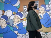 A woman wearing a face mask walks past a mural in Beijing, Friday, April 22, 2022. Officials in Shanghai promised Friday to ease anti-virus controls on truck drivers that are hampering food supplies and trade as they try to revive the local economy while millions of people are still confined to their homes.