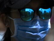 The skyline of Beijing is reflecting in the sunglasses of a woman wearing a face mask as she walks at a public park in Beijing, Thursday, April 14, 2022.