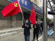 Residents carry the Communist Party flag and the Chinese national flag as others prepare to take part in the first round of mass COVID tests in the Jingan district of western Shanghai, China, Friday, April 1, 2022. As residents of western Shanghai start a four day lockdown for mass testing, some in eastern Shanghai about to end their lock down are being told they will be confined to their homes for at least 10 more days. It was the latest wrinkle in the lockdown of China's largest city as it struggles to eliminate an omicron-driven coronavirus outbreak under China's zero-COVID policy.