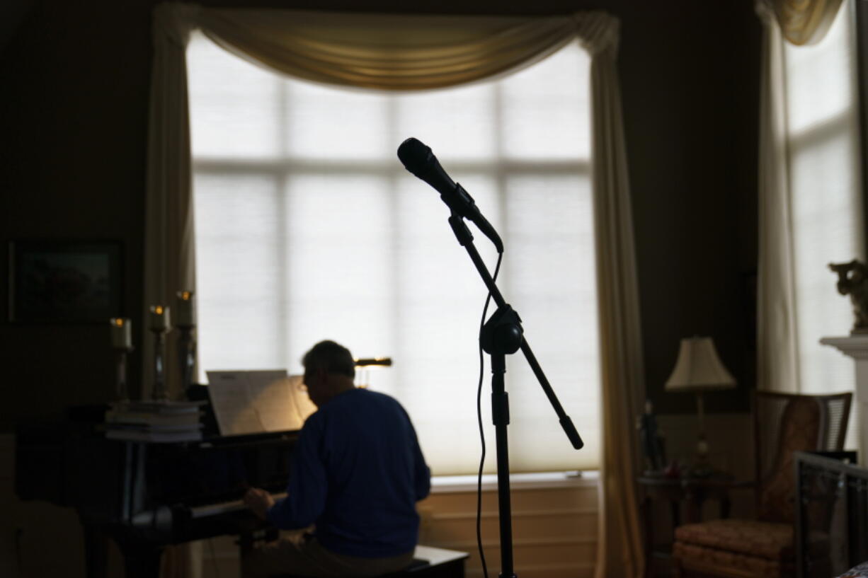 A microphone stands as David Lawyer plays the piano in his living room where his father, Neil Lawyer, would have sung along time to time in Bellevue, Wash., Sunday, March 20, 2022. The elder Lawyer died at age 84 on March 8, 2020, among the first residents of a Seattle area nursing home who succumbed to COVID-19 during the outbreak. At weddings, he joined his sons, grandson and nephew to serenade brides and grooms in a makeshift ensemble dubbed the Moose-Tones. Last October, when one of his granddaughters married, it marked the first family affair without Lawyer there to hold court. The Moose-Tones went on without him. "He would have just been beaming because, you know, it was the most important thing in the world to him late in life, to get together with family," David Lawyer says.