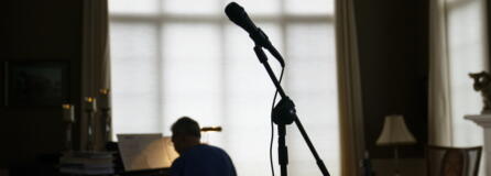 A microphone stands as David Lawyer plays the piano in his living room where his father, Neil Lawyer, would have sung along time to time in Bellevue, Wash., Sunday, March 20, 2022. The elder Lawyer died at age 84 on March 8, 2020, among the first residents of a Seattle area nursing home who succumbed to COVID-19 during the outbreak. At weddings, he joined his sons, grandson and nephew to serenade brides and grooms in a makeshift ensemble dubbed the Moose-Tones. Last October, when one of his granddaughters married, it marked the first family affair without Lawyer there to hold court. The Moose-Tones went on without him. "He would have just been beaming because, you know, it was the most important thing in the world to him late in life, to get together with family," David Lawyer says.