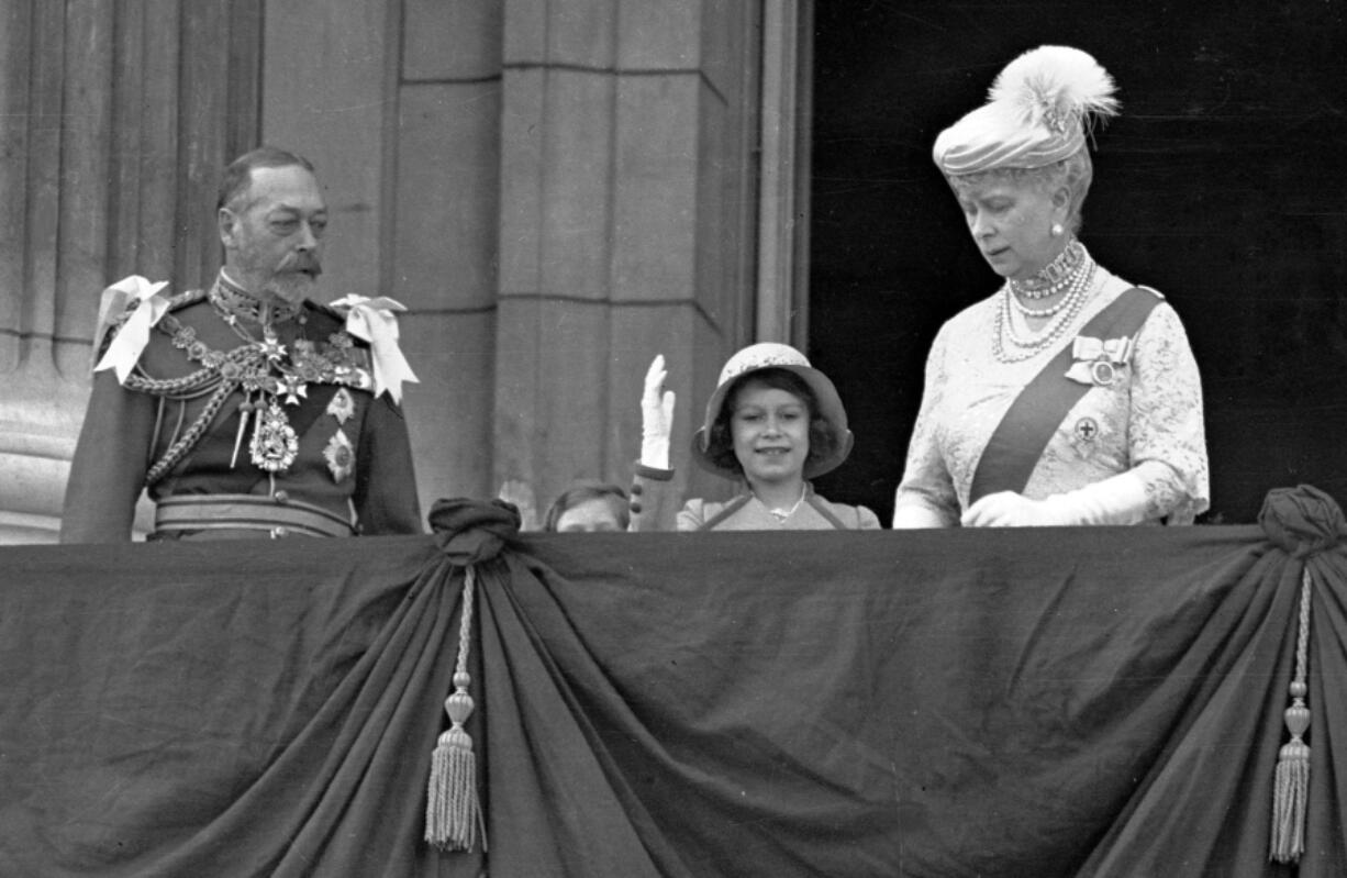 Princess Elizabeth, center, waves as she stands on the balcony of Buckingham Palace with her grandparents, King George V and Queen Mary, on May 6, 1935. Princess Margaret is just visible over the balcony edge.