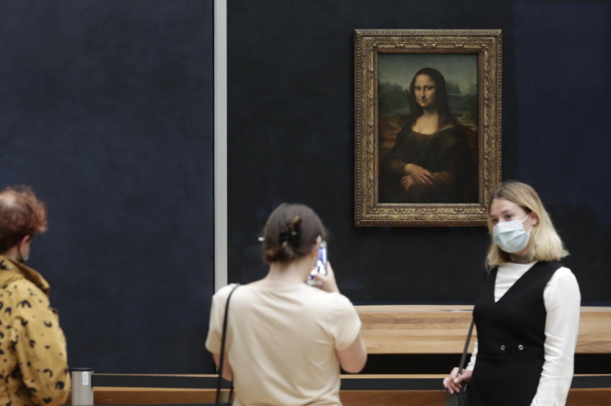 FILE - Visitors pose in front of Leonardo da Vinci's Mona Lisa in the Louvre museum, Wednesday, May, 19, 2021 in Paris. A man seemingly disguised as an old woman in a wheelchair threw a piece of cake at the glass protecting the Mona Lisa on Sunday May 29, 2022 at the Louvre Museum and shouted at people to think of planet Earth.