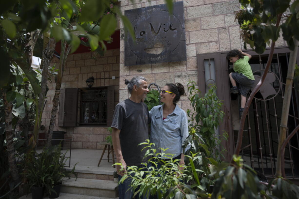 Kenae Totah, 5, right, plays while his parents Morgan Cooper, 41, center and Saleh Totah, right, pose for a photo in front of their restaurant, at the West Bank city of Ramallah, Monday, May 2, 2022.  The Israeli military body in charge of civilian affairs in the occupied West Bank has developed a new policy that would heavily regulate entry into the territory. Critics say it extends Israel's nearly 55-year military rule even further into every corner of Palestinian society. It would impose new restrictions on foreigners who work, study or volunteer in the West Bank and those who marry Palestinians.