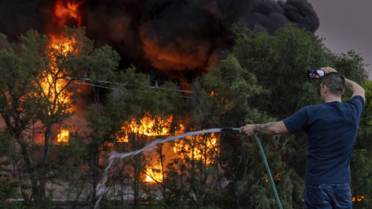 A man sprays down the roof of a neighboring building while also filming the scene of a three-alarm fire at Nox-Crete, Inc., at 1415 S. 20th Street in Omaha, Neb., Monday, May 30, 2022.