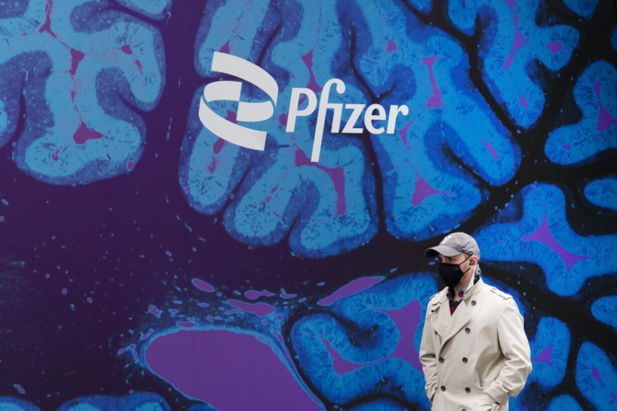 FILE - A man walks by Pfizer headquarters, Friday, Feb. 5, 2021 in New York.  Pfizer is spending more than $11 billion to buy the remaining portion of migraine treatment maker Biohaven Pharmaceuticals it does not already own. The New York drugmaker said Tuesday, May 10, 2022,  it will pay $148.50 in cash for each share of Biohaven, which makes Nurtec ODT for treating and preventing migraines and has another nasal spray under development.