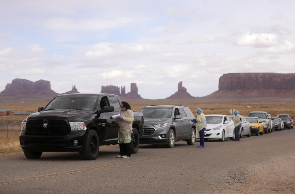 FILE - Korene Atene, a certified nursing assistant with the Monument Valley Health Center, gets information from people lined up to get tested for COVID-19 outside of the center in Oljato-Monument Valley, San Juan County, on Thursday, April 16, 2020. In a pandemic that has seen sharp divides between urban and rural vaccination rates nationwide, Arizona is the only state where rural vaccine rates outpaced more populated counties, according to a recent report from the U.S. Centers for Disease Control and Prevention.