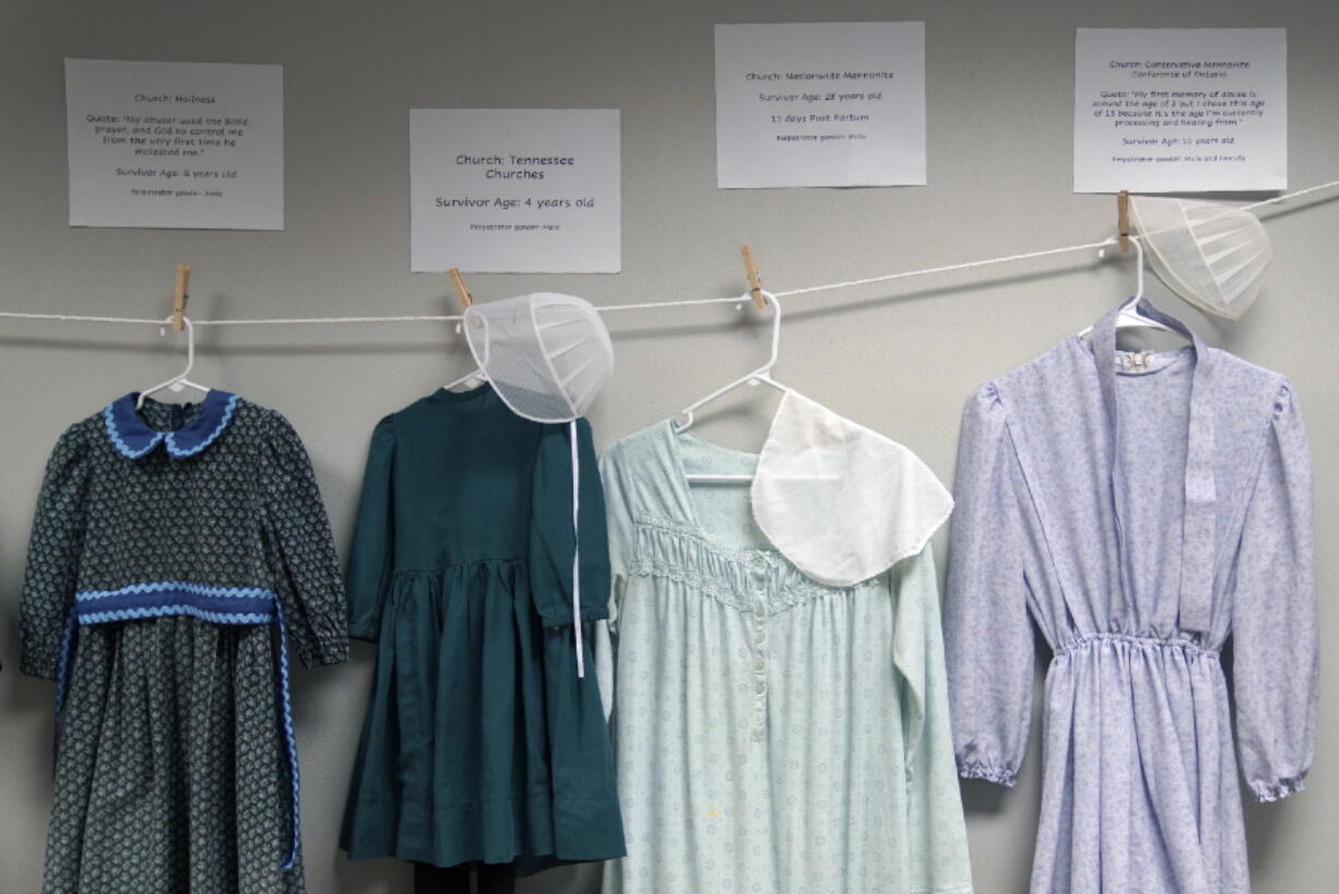 Dresses donated by sexual assault survivors from Amish and other plain-dressing religious groups hang on a clothesline beneath a description of each survivors' age and church affiliation, on Friday, April 29, 2022, in Leola, Pa. The exhibit's purpose was to show that sexual assault is a reality among children and adults in such groups. Similar exhibits held nationwide aim to shatter the myth that abuse is caused by a victim's clothing choice.