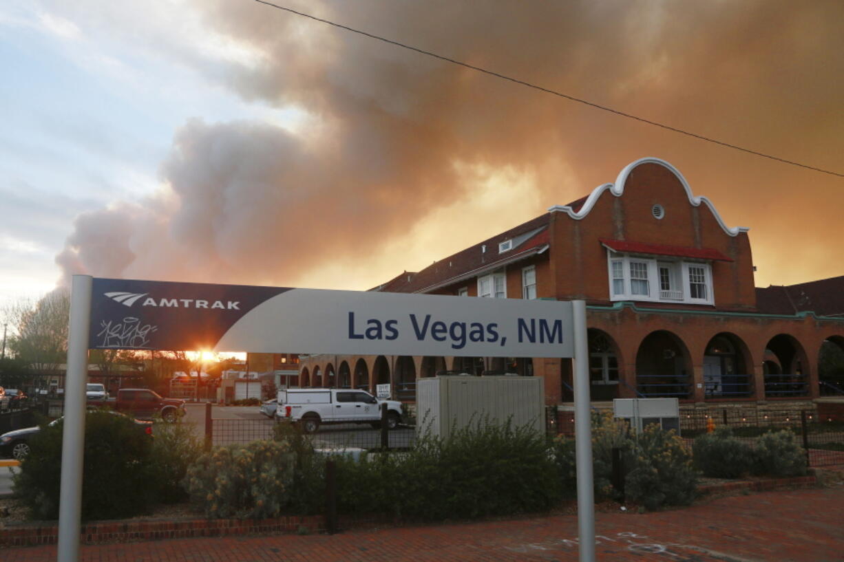 A sunset seen through a wall of wildfire smoke from the Amtrak train station in Las Vegas, N.M., on Saturday, May 7, 2022. The Casta?eda Hotel, right, hosted meals for residents and firefighters this week with sponsorships from restaurants and other businesses.