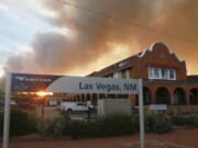 A sunset seen through a wall of wildfire smoke from the Amtrak train station in Las Vegas, N.M., on Saturday, May 7, 2022. The Casta?eda Hotel, right, hosted meals for residents and firefighters this week with sponsorships from restaurants and other businesses.