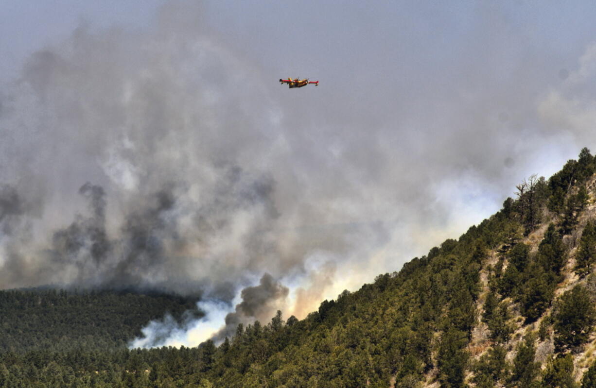 A firefighting plane flies over a plume of smoke near Las Vegas, N.M. on Wednesday, May 4, 2022. The fire has torched 250 square miles (647 square kilometers) over the last several weeks.