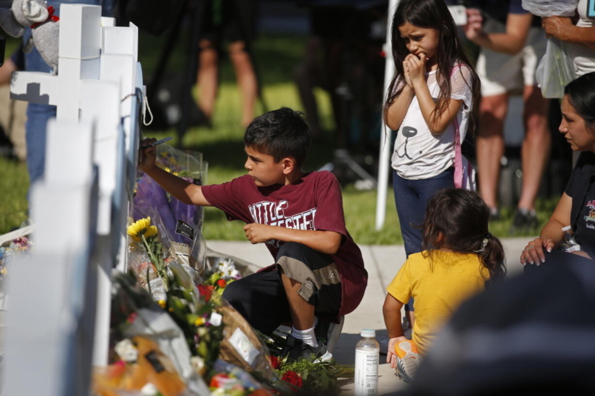 A child writes a message on a cross at a memorial site for the victims killed in this week's elementary school shooting in Uvalde, Texas, Thursday, May 26, 2022.