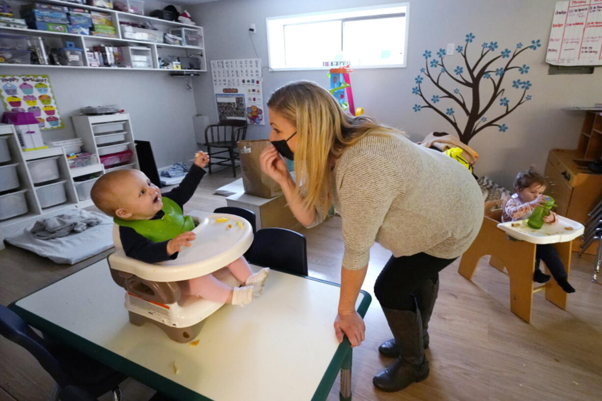 FILE - Amy McCoy signs to a baby about food as a toddler finishes lunch behind at her Forever Young Daycare facility, Monday, Oct. 25, 2021, in Mountlake Terrace, Wash. According to a report released by the Centers for Disease Control and Prevention on Tuesday, May 24, 2022, U.S. births bumped up in 2021, but the number of babies born was still lower than before the coronavirus pandemic.