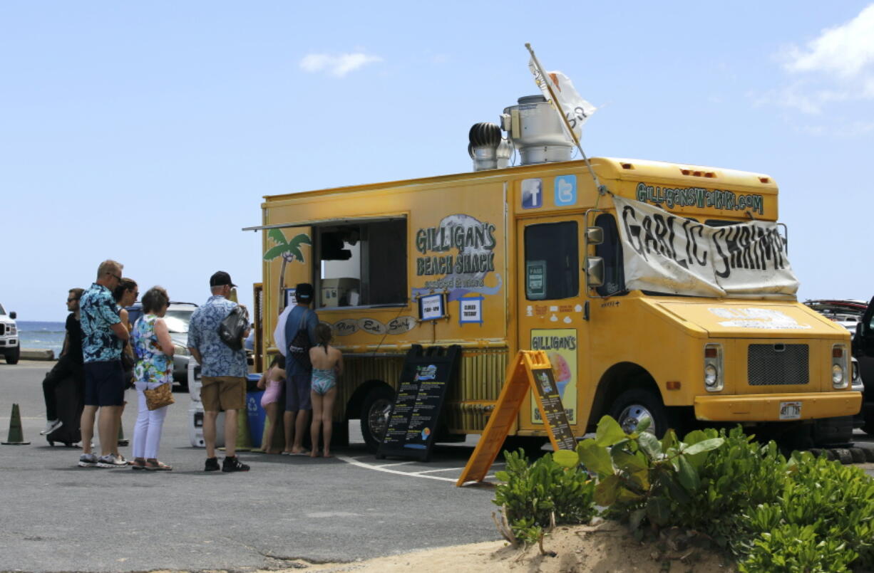 People line up at a food truck parked near Waikiki Beach in Honolulu, Monday, May 23, 2022. A COVID surge is under way that is starting to cause disruptions as schools wrap up for the year and Americans prepare for summer vacations. Case counts are as high as they've been since mid-February and those figures are likely a major undercount because of unreported home tests and asymptomatic infections. But the beaches beckoned and visitors have flocked to Hawaii, especially in recent months.