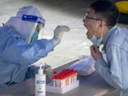 FILE - A worker in a protective suit swabs a man's throat for a COVID-19 test at a testing site in an office complex in Beijing, Friday, April 29, 2022. The World Health Organization on Thursday, May 5, 2022 is estimating that nearly 15 million people were killed either by the coronavirus or by its impact on overwhelmed health systems in the past two years, more than double the official death toll of 6 million.