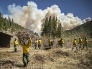 Firefighters with Structure Group 4 clear brush and debris away from cabins along Highway 518 near the Taos County line in New Mexico, May 13, 2022, while fire rages over the nearby ridge.