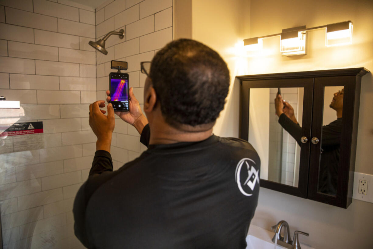 Ben Poles, owner of Rest Assured Inspections, takes a photo and checks the temperature of the water in the shower during a home inspection.