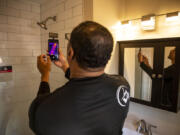 Ben Poles, owner of Rest Assured Inspections, takes a photo and checks the temperature of the water in the shower during a home inspection.