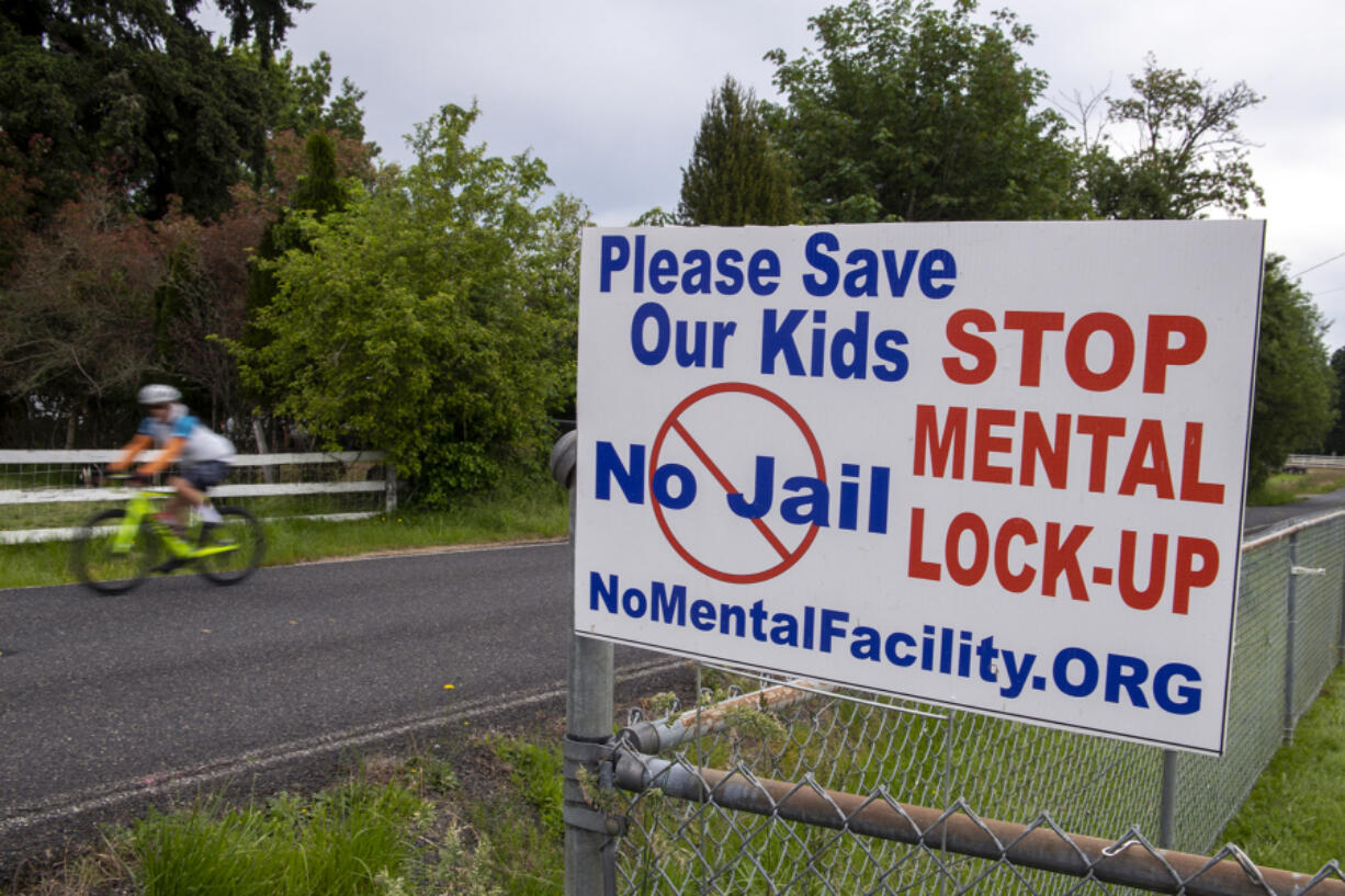 A bicyclist passes a sign protesting a proposed behavioral health facility near Northeast 50th Avenue and Northeast 159th Street.