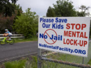 A bicyclist passes a sign protesting a proposed behavioral health facility near Northeast 50th Avenue and Northeast 159th Street.