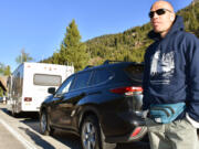 Muris Demirovic waits by his rental car outside Yellowstone National Park for the entrance gate to open, Wednesday June 22, 2022, near Wapiti, Wyo. Demirovic said he was supposed to leave the area  earlier in the week but extended his trip to get in the park when it partially reopened after flood damage forced it to close last week.